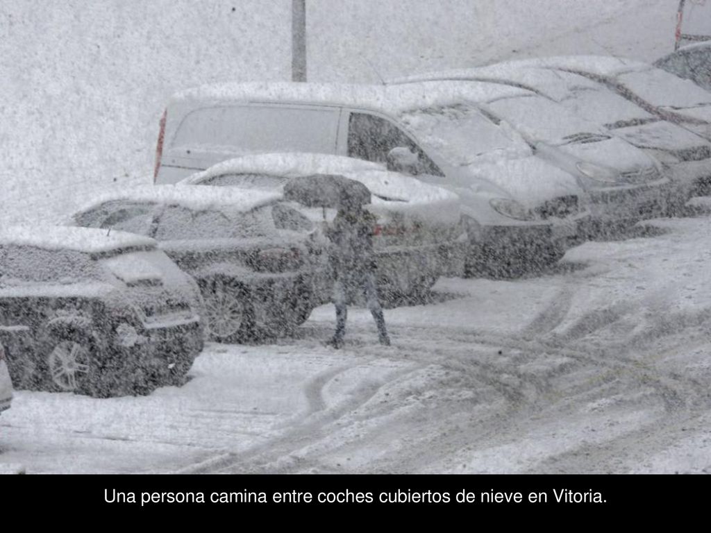 Una persona camina entre coches cubiertos de nieve en Vitoria.
