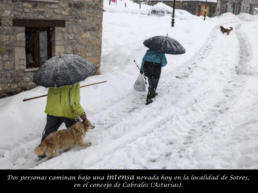 Dos personas caminan bajo una intensa nevada hoy en la localidad de Sotres, en el concejo de Cabrales (Asturias).