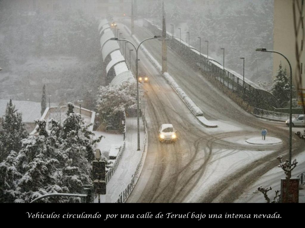 Vehículos circulando por una calle de Teruel bajo una intensa nevada.