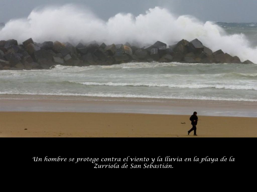 Un hombre se protege contra el viento y la lluvia en la playa de la Zurriola de San Sebastián.
