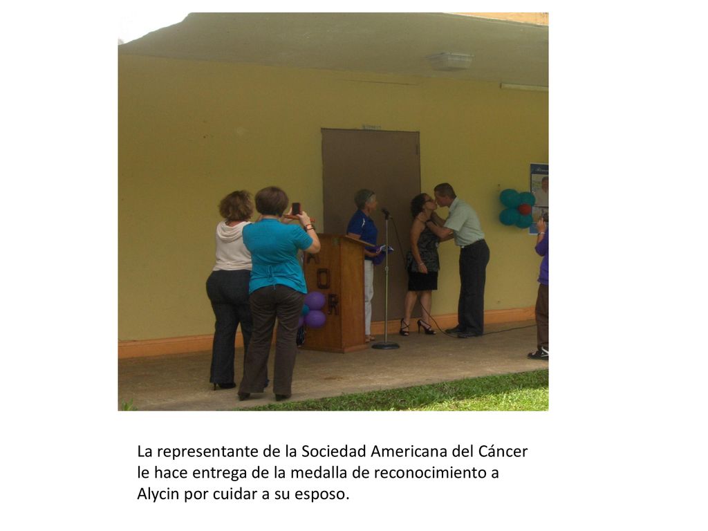 La representante de la Sociedad Americana del Cáncer le hace entrega de la medalla de reconocimiento a Alycin por cuidar a su esposo.