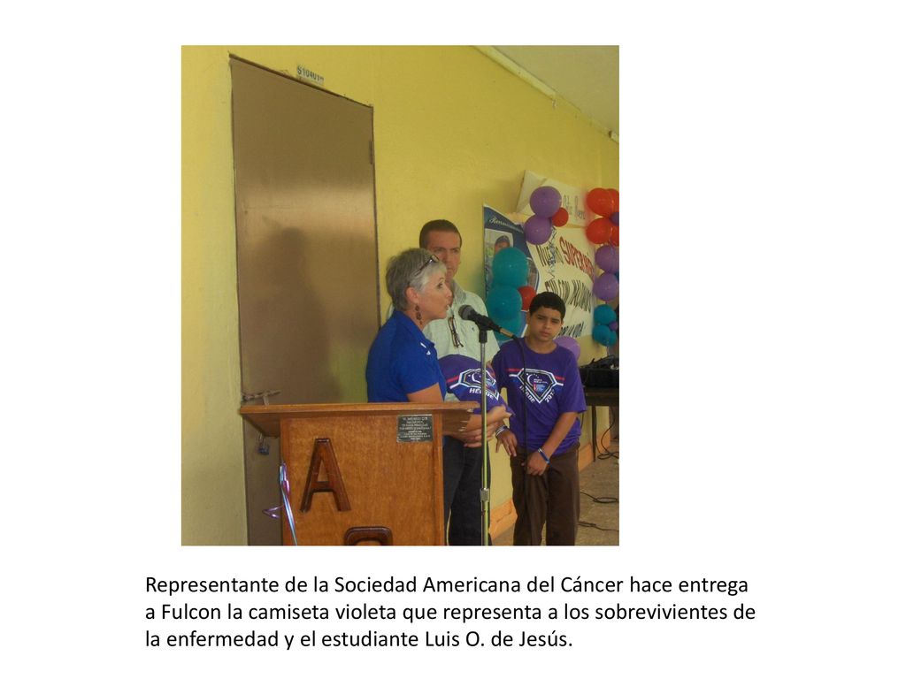 Representante de la Sociedad Americana del Cáncer hace entrega a Fulcon la camiseta violeta que representa a los sobrevivientes de la enfermedad y el estudiante Luis O.