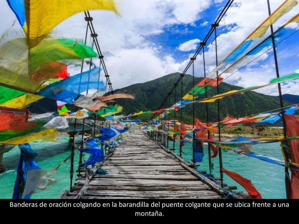 Banderas de oración colgando en la barandilla del puente colgante que se ubica frente a una montaña.