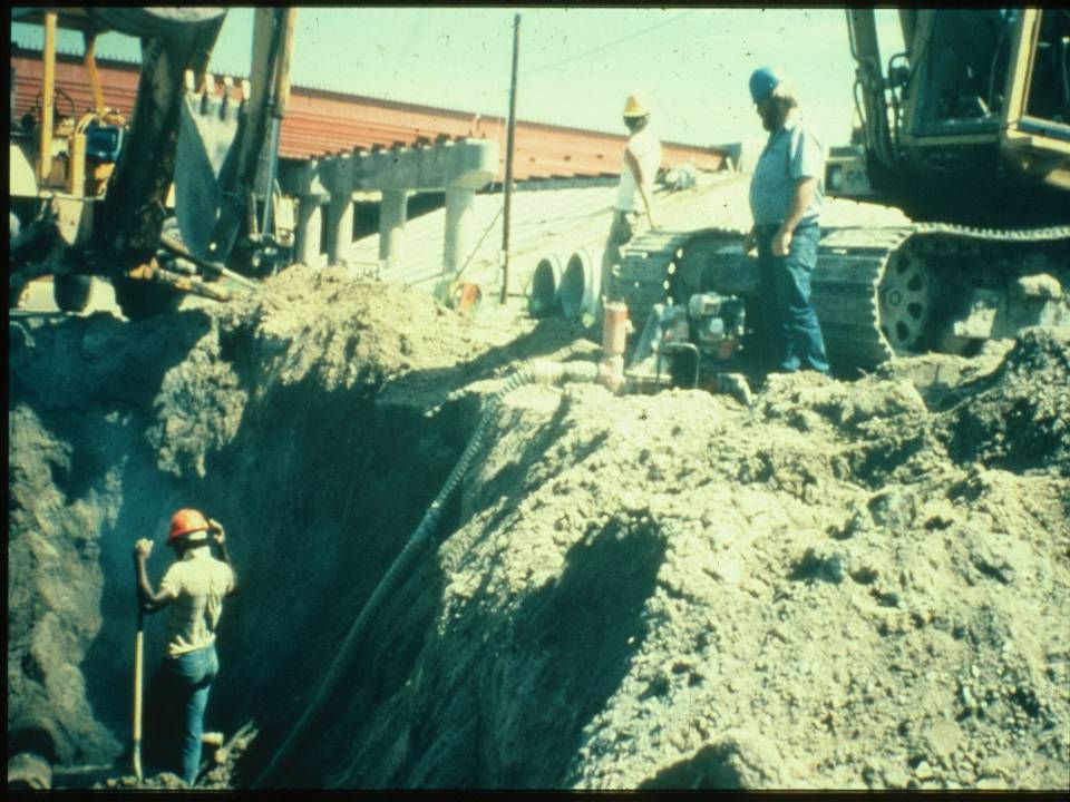 Una zanja sin apuntalamiento con un backhoe y un track hoe y una bomba para la eliminación de agua.