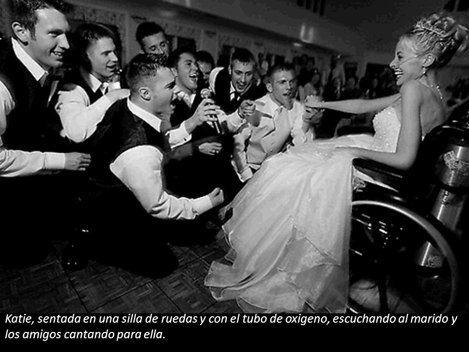 Katie, sentada en una silla de ruedas y con el tubo de oxigeno, escuchando al marido y los amigos cantando para ella.